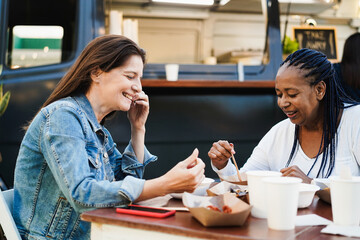 Multiracial women eating at food truck restaurant outdoor - Focus on african female ear