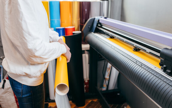 Female hands holding yellow printable material on alarge format printing plotter. Graphic design and  advertising concept.