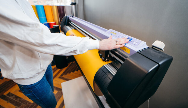 Female hands holding yellow printable material on alarge format printing plotter. Graphic design and  advertising concept.