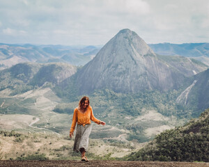 mulher com blusa amarela caminhando com montanhas ao fundo em Pancas, Espírito Santo