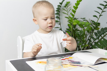 A little boy paints with watercolor paints on a table.