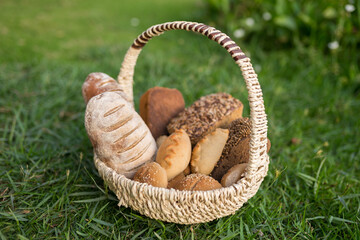 Assorti of brown and white homemade bread in wicker basket standing on the grass
