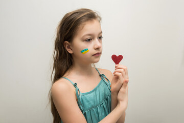 Little girl with the flag of Ukraine on her face and a heart in her hand. Free Ukraine.Love for...