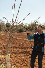young man working in the field pruning fruit trees. the soil is reddish in color. non-professional model, authentic male farmer.