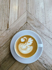 A mug of flat white or latte art coffee on a wooden table. Coffee art. Directly above. Swan shape