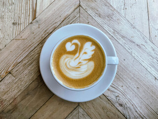 A mug of flat white or latte art coffee on a wooden table. Coffee art. Directly above. Swan shape