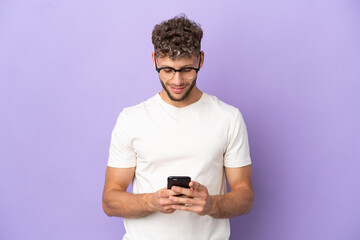 Delivery caucasian man isolated on purple background sending a message with the mobile