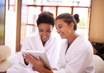 Checking in At the spa. Shot of two friends in bathrobes using a digital tablet at a spa.