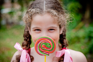 Portrait of beautiful girl with pigtails showing a lollipop to the camera, focus on the lollipop