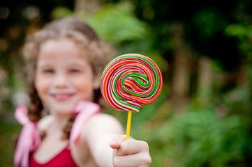 Portrait of beautiful girl with pigtails showing a lollipop to the camera, focus on the lollipop