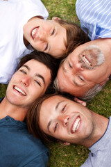 Fototapeta premium Laughing together through the ages. Father and sons lying down on the grass with their heads beside one another.