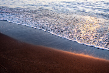 Black magnetite sand and sea waves under sunset rays, copper highlights on sand, blurred seascape background