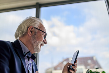 Low angle portrait of smiling mature businessman business leader holding smart phone senior manager...