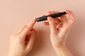 Checking blood sugar level with lancet and glucometer at home. Blood glucose meter. Woman hand, beige background