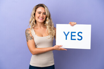 Young Brazilian woman isolated on purple background holding a placard with text YES with happy expression