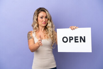 Young Brazilian woman isolated on purple background holding a placard with text OPEN making a deal