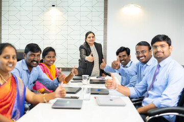 smiling confident corporate employees with uniform showing thumbs up by looking at camera at conference room during business meeting - concept of teamwork, successful and achievement.