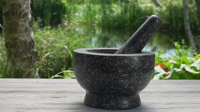 Hand is putting peppers and fresh spices into a grey stone mortar in slow motion