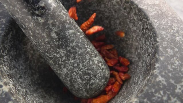 Close-up of red cayenne pepper pods falling and bouncing in the stone mortar