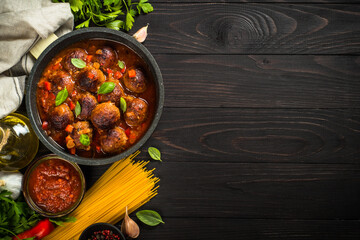 Meatballs in tomato sauce and raw pasta on dark wooden table. Food cooking background. Top view with copy space.