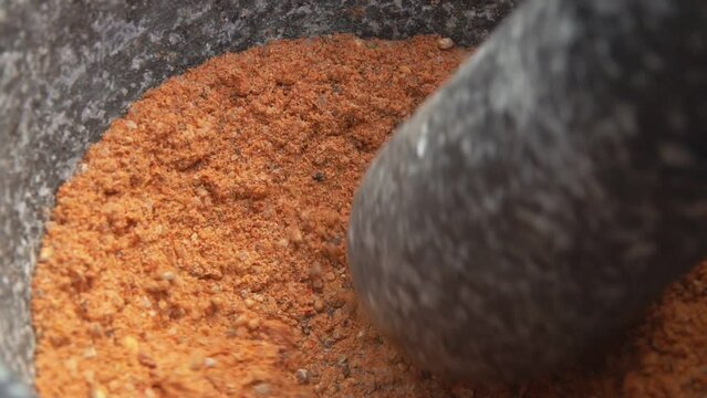 Super close-up of pestle grinding spices and peppers in mortar into the powder