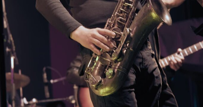 Man saxophonist at a concert plays the saxophone and dances. Live musical performance and virtuosity of playing a brass musical instrument. It dark, colored spotlights are shining around