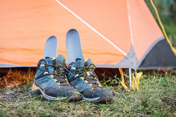 A pair of wet and dirty hiking boots are drying near the tent with the insole sticking out - obrazy, fototapety, plakaty