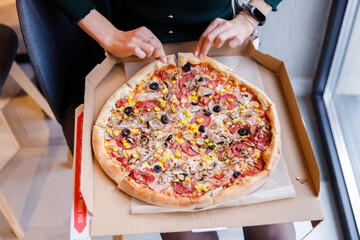 young pretty girl students eat in a cafe hot pizza with olives, sausage, corn and bacon