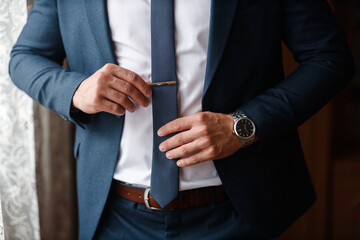 stylish male businessman in a dark jacket with a tie and in a white shirt fastens buttons on a gray...