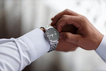 hands of an adult man in a white dress shirt wind up a stylish swiss watch, close-up without a face