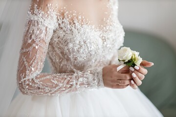 girl bride in a luxurious dress embroidered with beads and sequins holds a boutonniere in her hands...