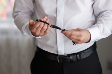 an adult man in a white dress shirt holds a wooden rosary in his hands, without a face close-up