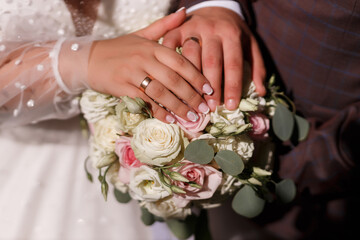 Obraz na płótnie Canvas hands of a man of the bridegroom and the girl of the bride with gold wedding rings close-up on a wedding bouquet of roses