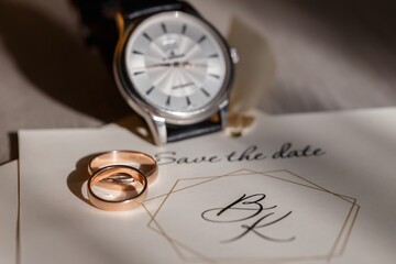 gold wedding rings lie on top of each other on an invitation card near a classic silver mechanical...