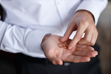 the groom in a white classic shirt with sleeves holds wedding gold rings on his palm, close-up without a face