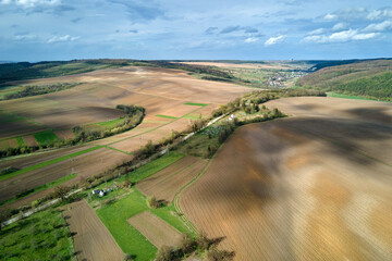 Aerial view of plowed agricultural fields with cultivated fertile soil prepared for planting crops between green woods in spring