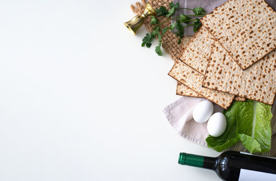 Layout of  Traditional Matzah prepared for Passover with egg, bottle of wine, glass, green salad and parsley on white background. top view. Spring Holiday of Jewish people. Fasting time