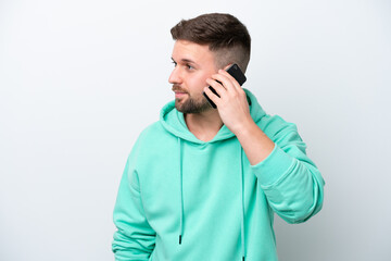 Young caucasian man isolated on white background keeping a conversation with the mobile phone with someone