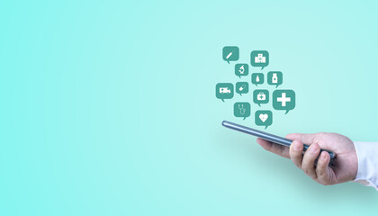 A hand holding a mobile phone with a speech bubble of healthcare and medical icon on a turquoise background with copy space.