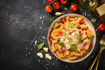 Italian pasta alla arrabiata with basil and parmesan on black stone table. Fusilli pasta with tomato sauce. Top view with copy space.