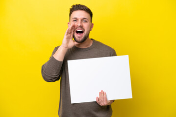 Young caucasian man isolated on yellow background holding an empty placard and shouting