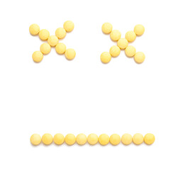 Dead smiley made of yellow pills on white background