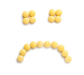 Sad smiley made of yellow pills on white background