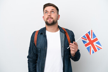 Young caucasian man holding an United Kingdom flag isolated on white background and looking up
