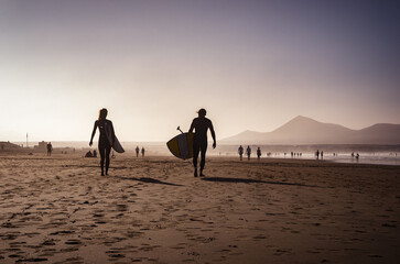 Couple walking on the beach with surfboard nad paddleboard. Water sports. Surfing concept. Paddleboarding. Active couple.