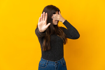 Teenager Brazilian girl isolated on yellow background making stop gesture and covering face