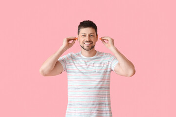 Handsome man putting ear plugs on pink background