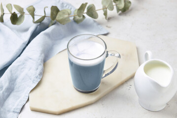 Glass cup of delicious Charcoal Latte and jug with milk on light table