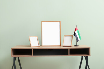 Blank frames and UAE flag on table near green wall