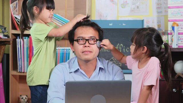 Funny girls doing makeup and hair for dad. Work from home. Daughters disturbs father working remotely because of covid epidemic on table with laptop at home.